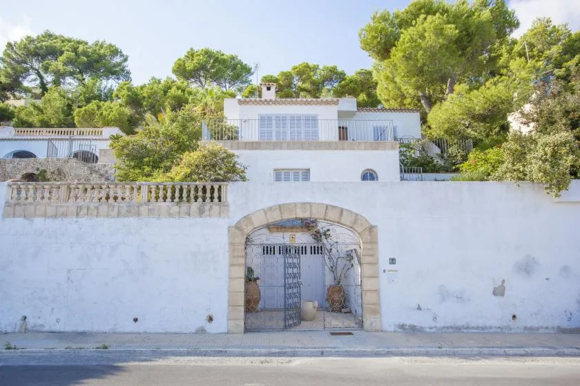 A white building stands behind a high wall with an arched metal gate.