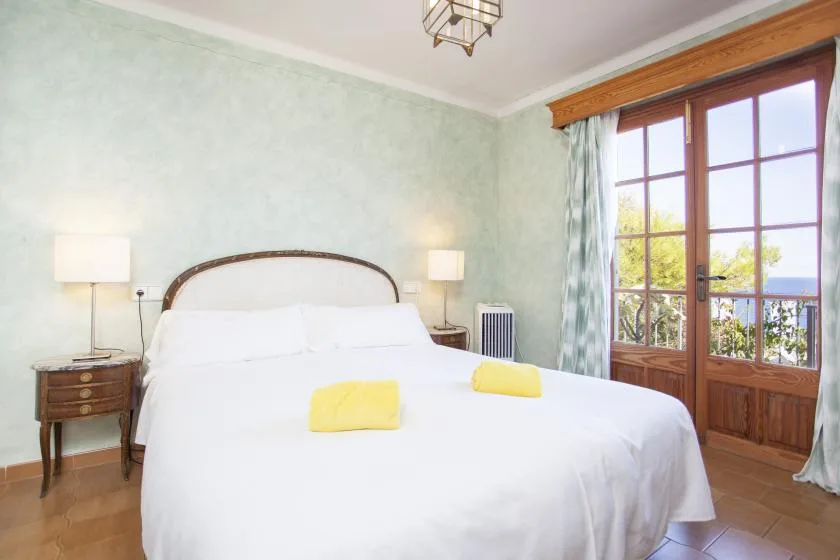 A bright bedroom with a large bed and tall wooden-framed windows.