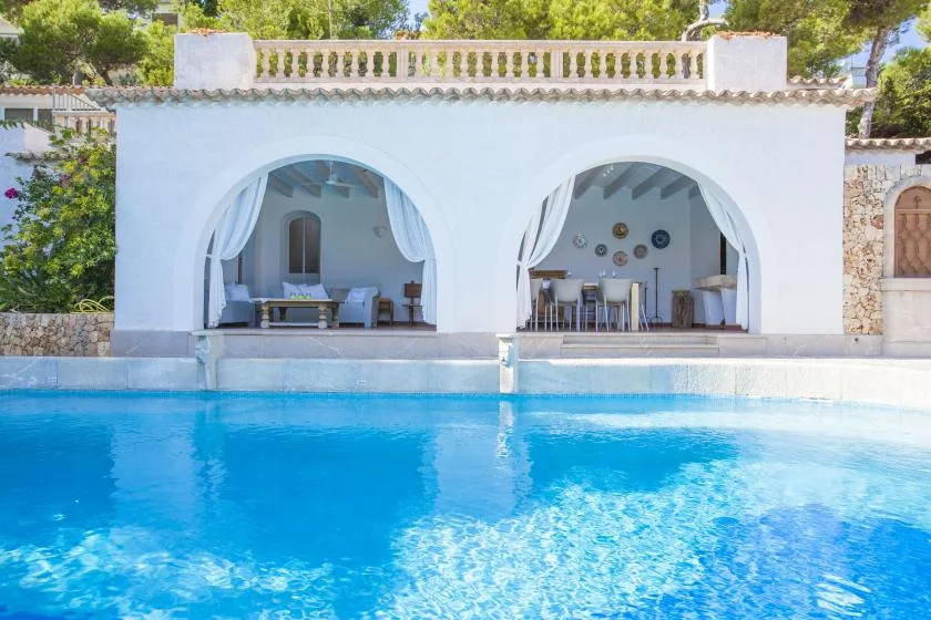 A blue swimming pool sits in front of a white building with two arched openings.