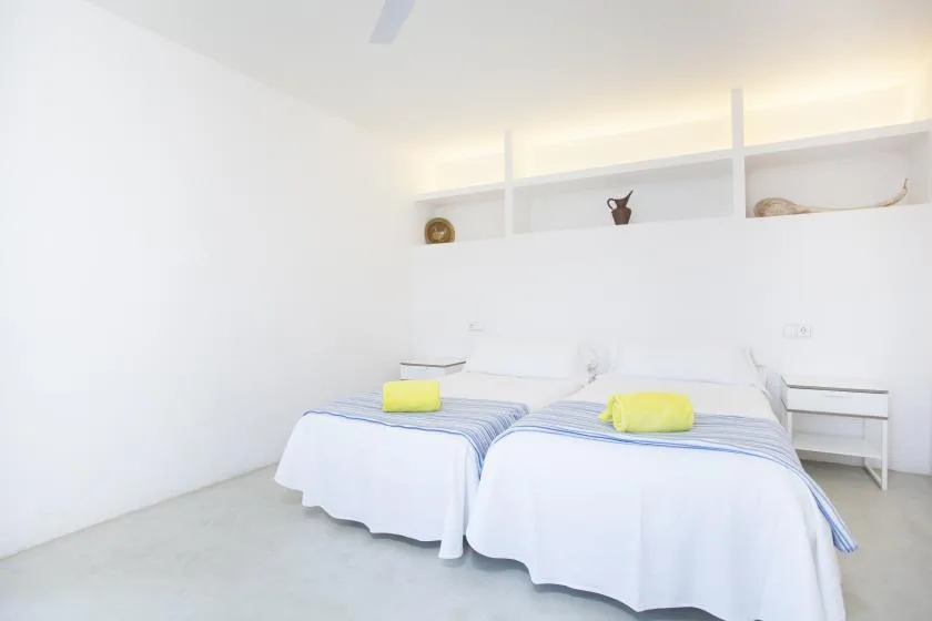 A bright bedroom with two beds beneath a wall shelf.