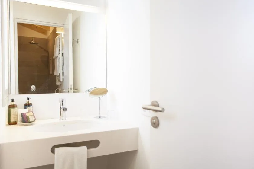 A bright bathroom with a white vanity, mirror, and shower visible in the reflection.