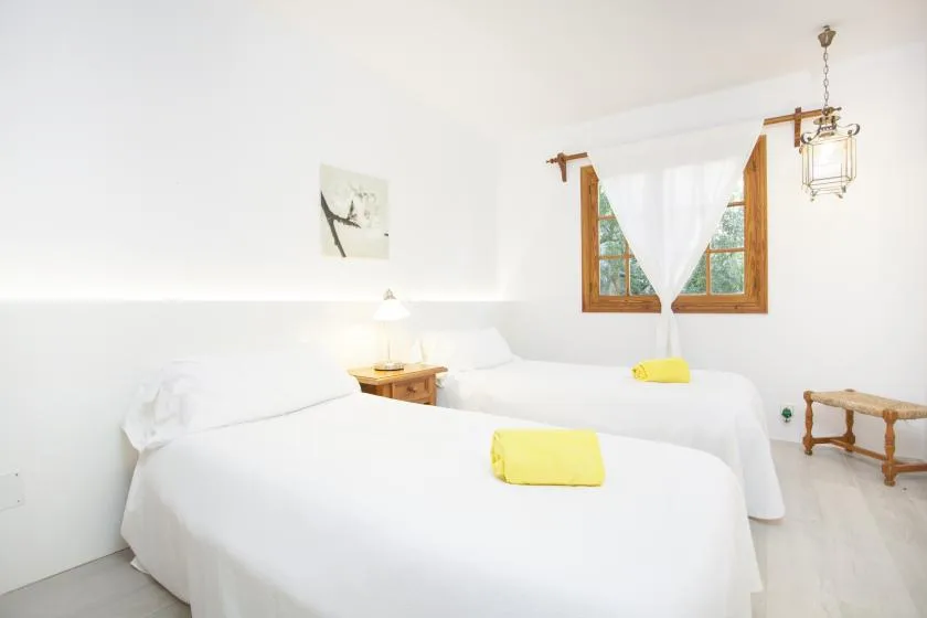 A bright bedroom with two beds, yellow towels, and a wooden-framed window.