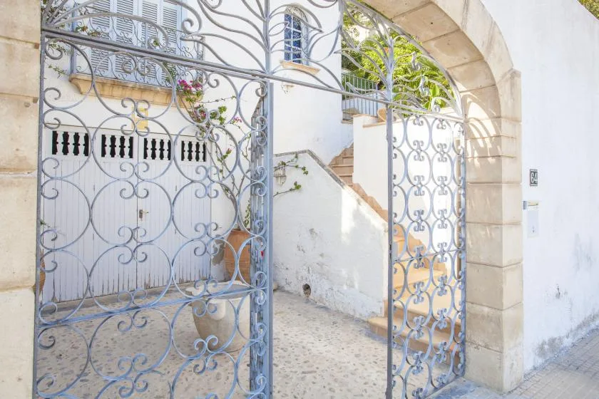 An ornate metal gate opens onto a paved courtyard beside a white building.