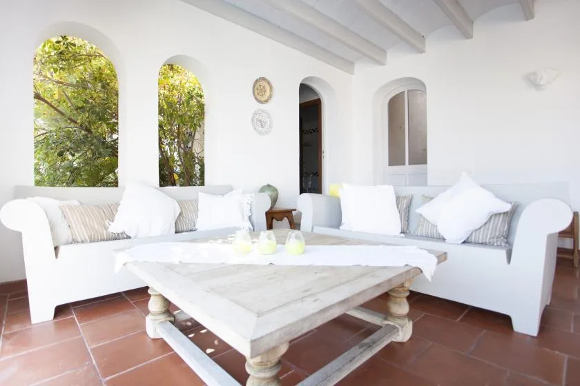 A bright living room with white seating arranged around a low wooden coffee table.