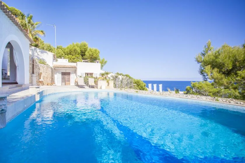 An outdoor swimming pool beside a white building, with the sea visible beyond.