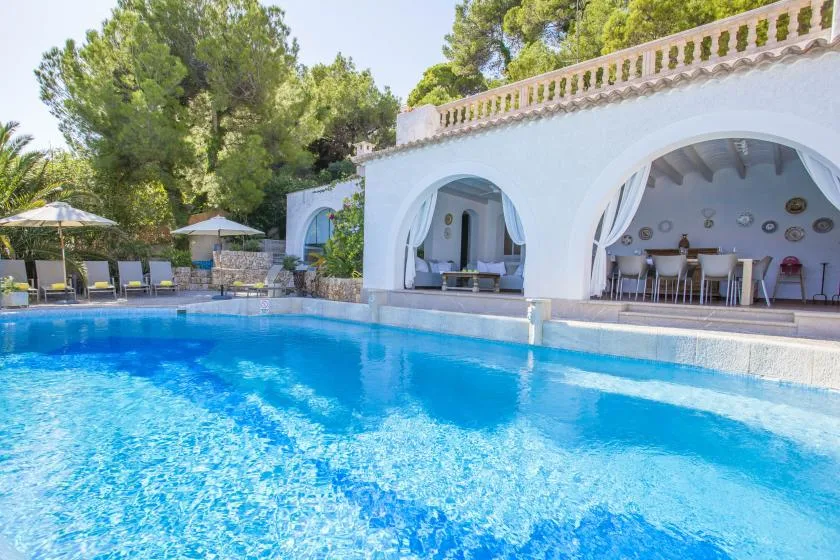 A swimming pool sits in front of an arched outdoor dining area.