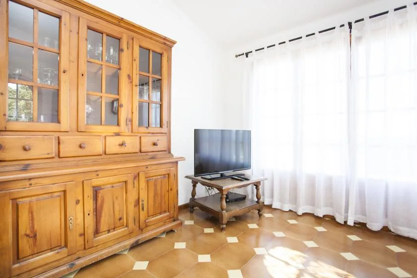 A living room with a wooden cabinet, television, and bright curtained window.