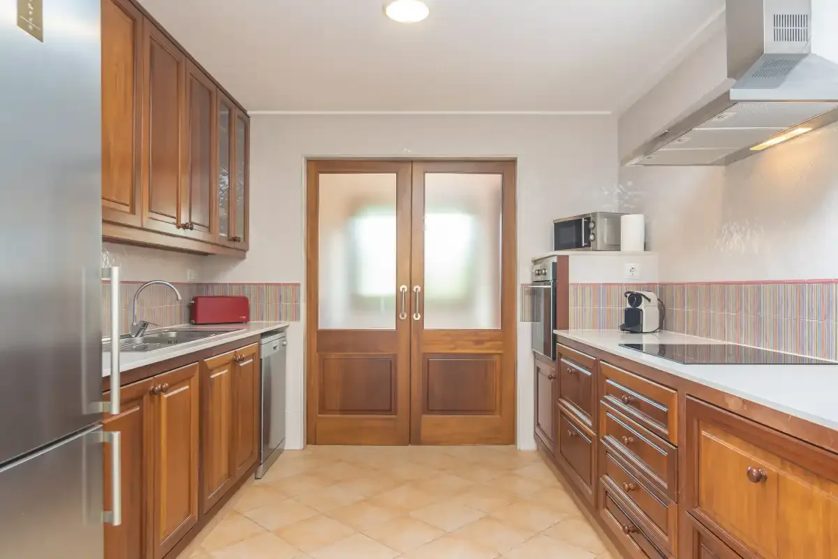 Una cocina con armarios de madera, encimeras y una puerta doble al fondo.