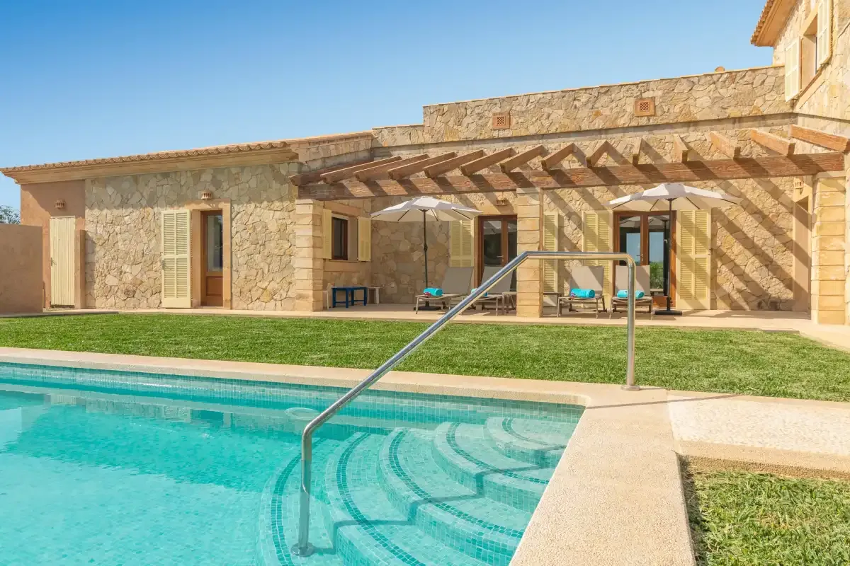 Una casa de piedra y un patio sombreado junto a una piscina.
