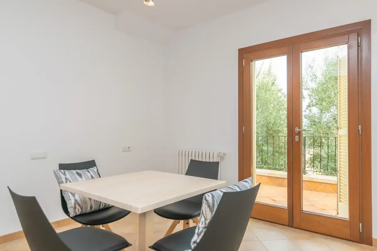 Un comedor luminoso tiene una mesa rectangular y puertas acristaladas que dan a un balcón.