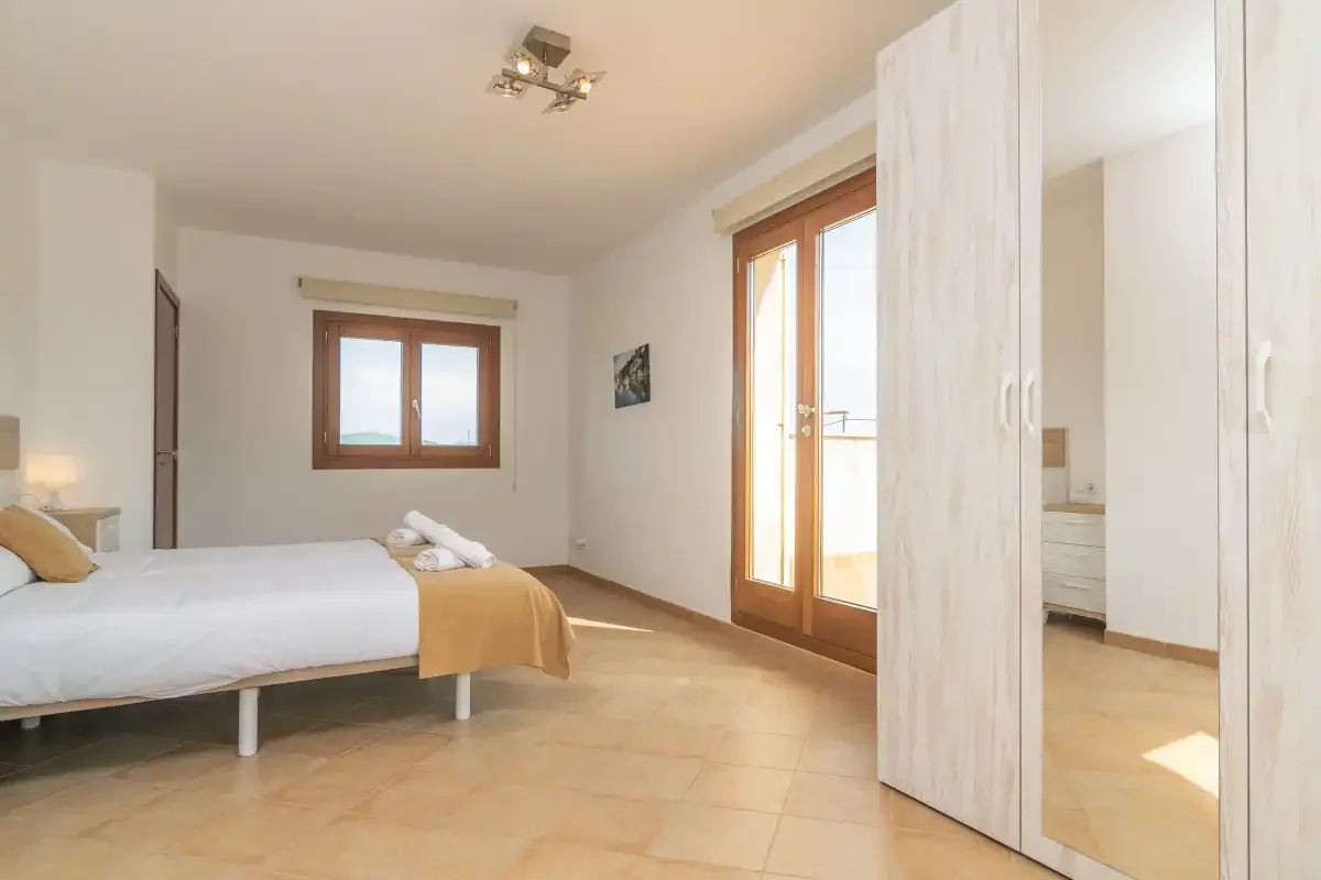 Un dormitorio luminoso con una cama junto a armarios altos con espejo.