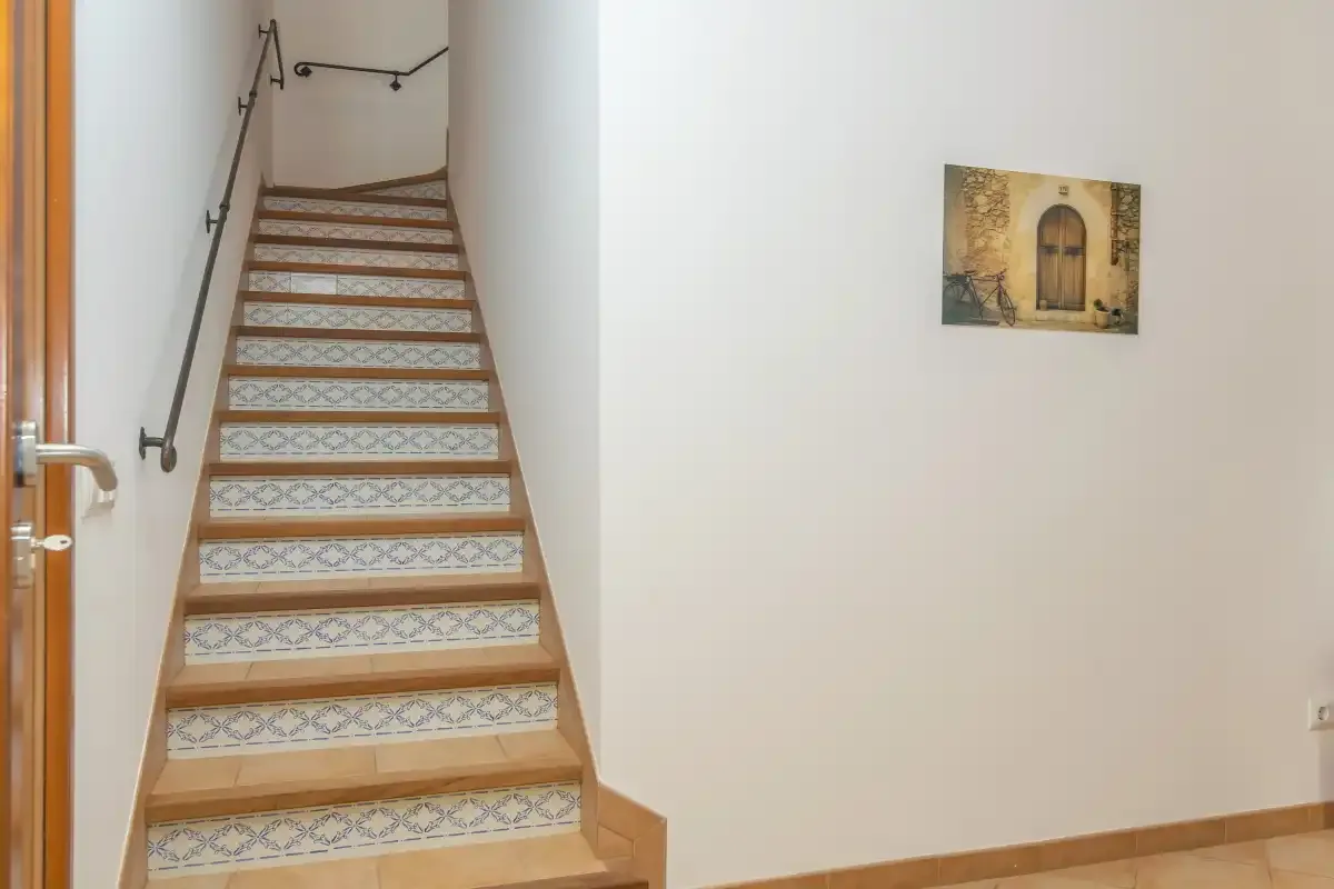Una escalera con contrahuellas de azulejos estampados sube junto a una pared lisa.