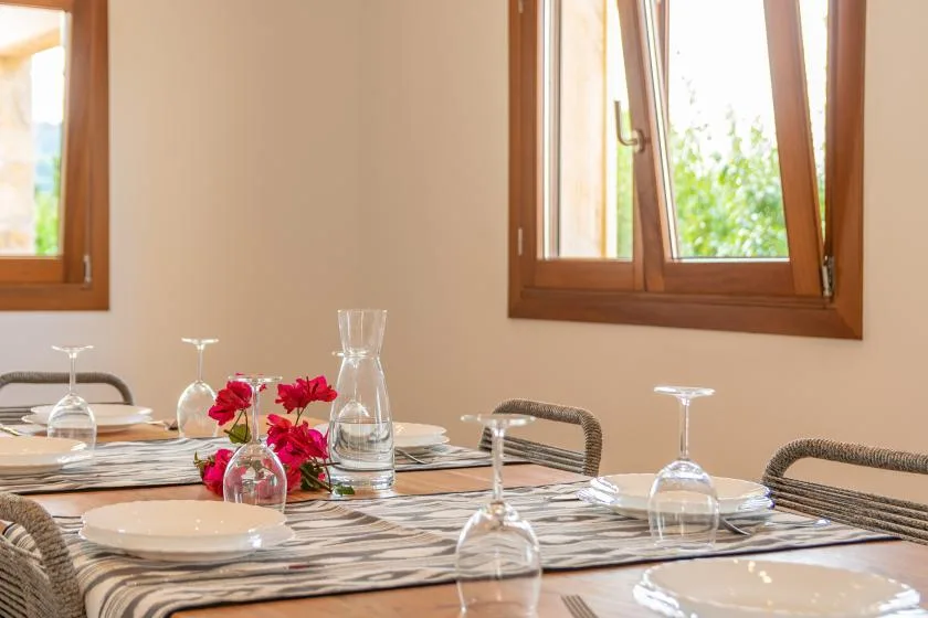 Comedor con una mesa puesta y flores junto a ventanas abiertas.