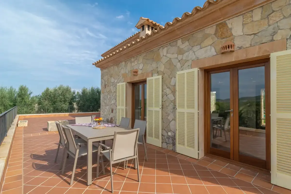 Una casa de piedra da a una terraza de baldosas terracota con asientos al aire libre.