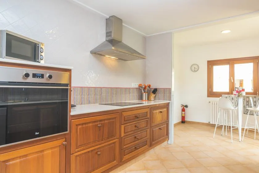 Una cocina luminosa con gabinetes de madera, horno y comedor junto a la ventana.