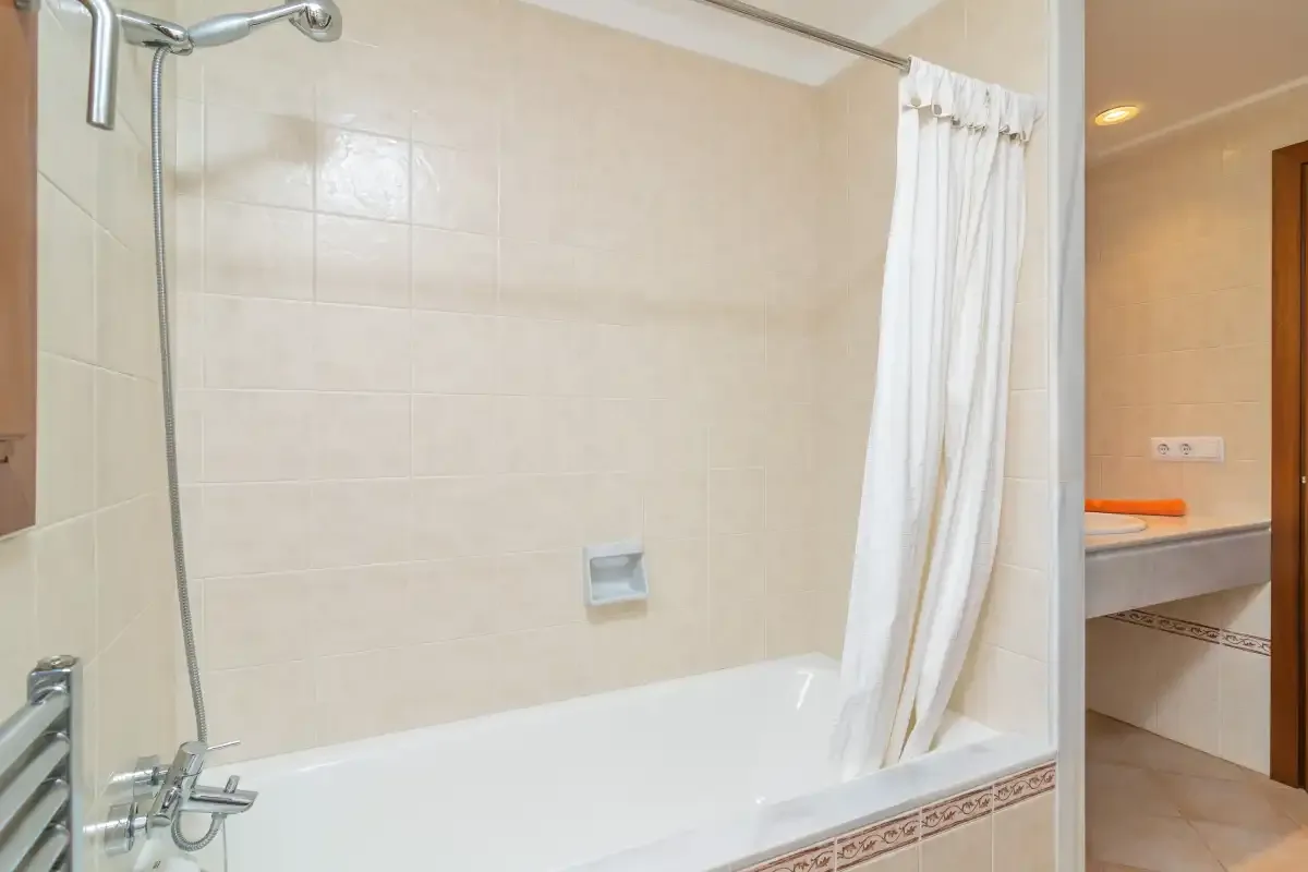 Un baño alicatado con bañera, grifería de ducha y una cortina blanca.