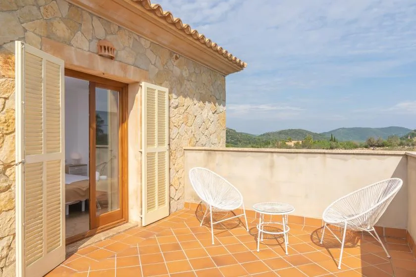 Una terraza exterior con suelo de baldosas y dos asientos blancos da a colinas lejanas.