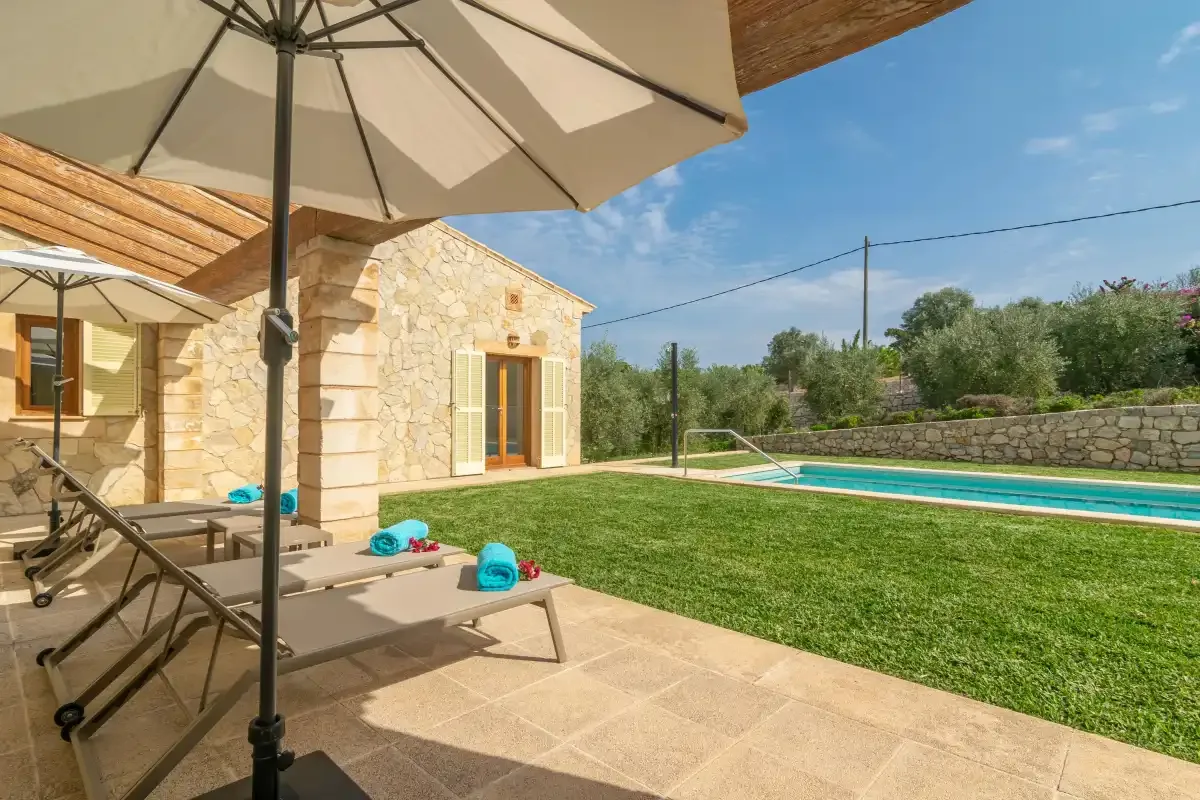 Una casa de piedra da a un patio con tumbonas junto a una piscina.