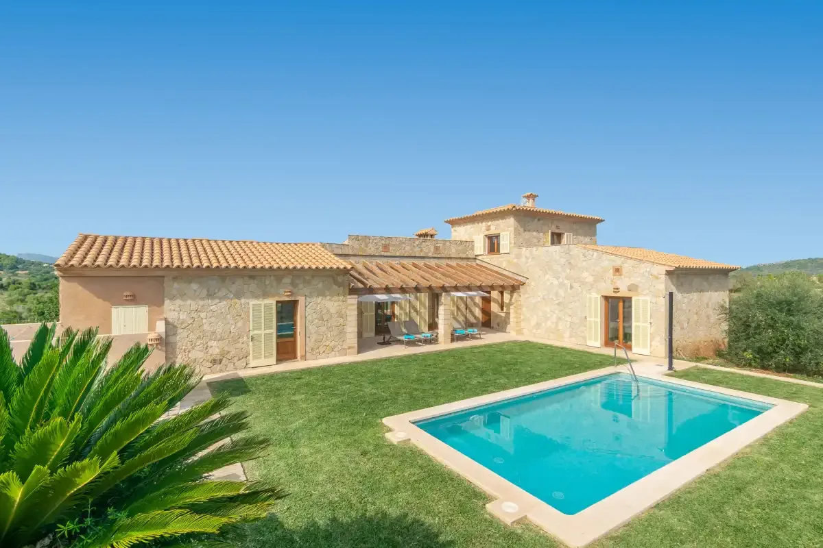 Una casa de piedra se encuentra junto a una piscina turquesa y un césped verde.