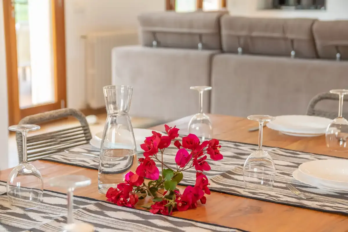 Una mesa de comedor con flores rojas está frente a una zona de estar.