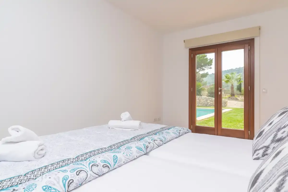 Un dormitorio luminoso con una colcha estampada y puertas de vidrio que dan a un jardín.