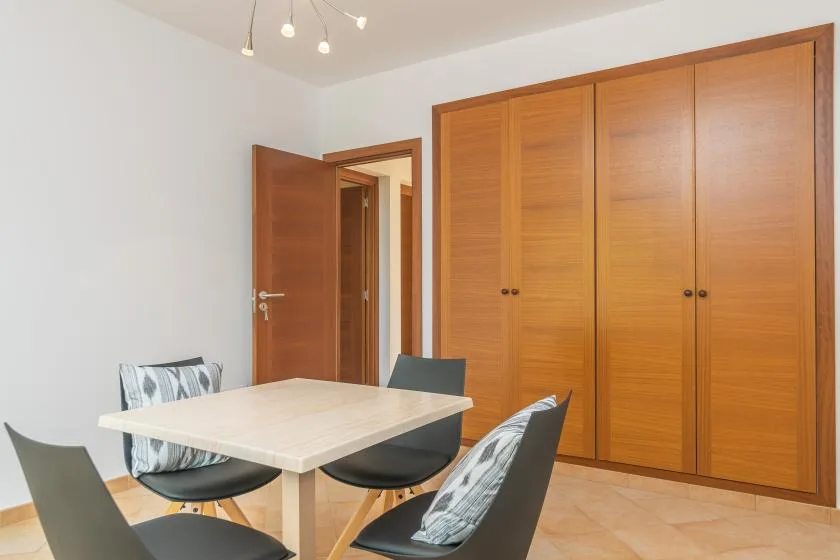 Comedor con una mesa clara y sillas junto a armarios de madera.