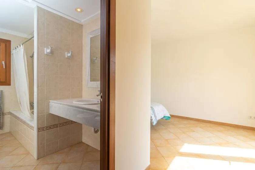Un baño alicatado con cortina de ducha y lavabo da a una habitación contigua luminosa.