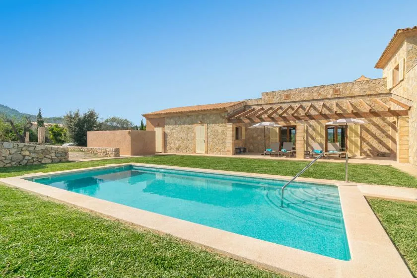 An outdoor swimming pool sits beside a stone house and shaded patio.