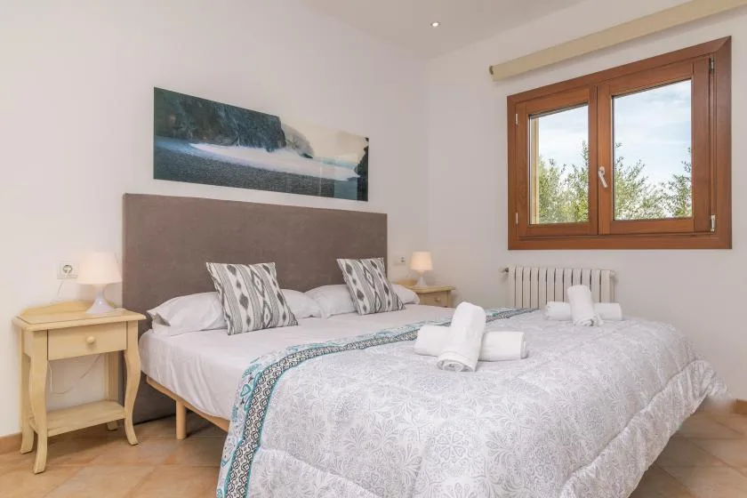 Un dormitorio luminoso con una cama doble y una ventana con marco de madera.