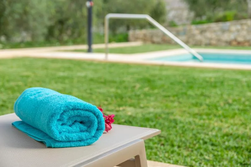 Una toalla turquesa está sobre una tumbona junto a una piscina y el césped.