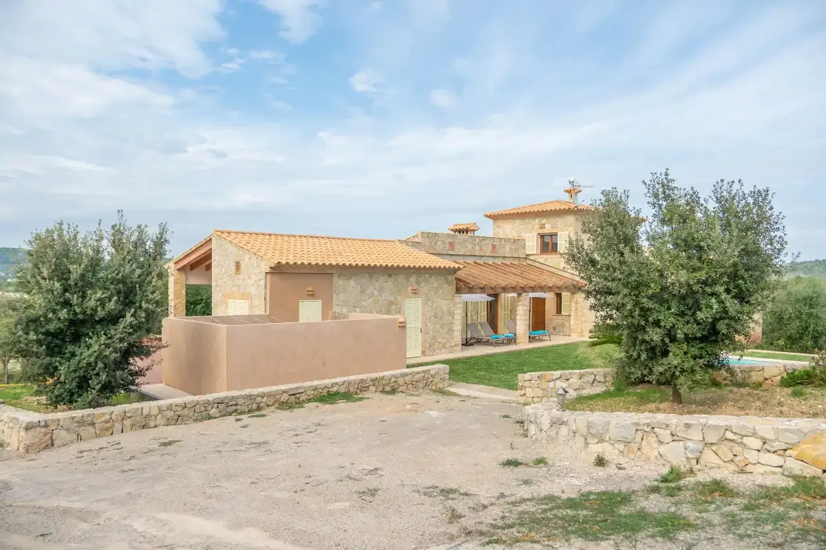 Una casa de piedra con tejados de tejas está junto a un camino de grava y un césped verde.