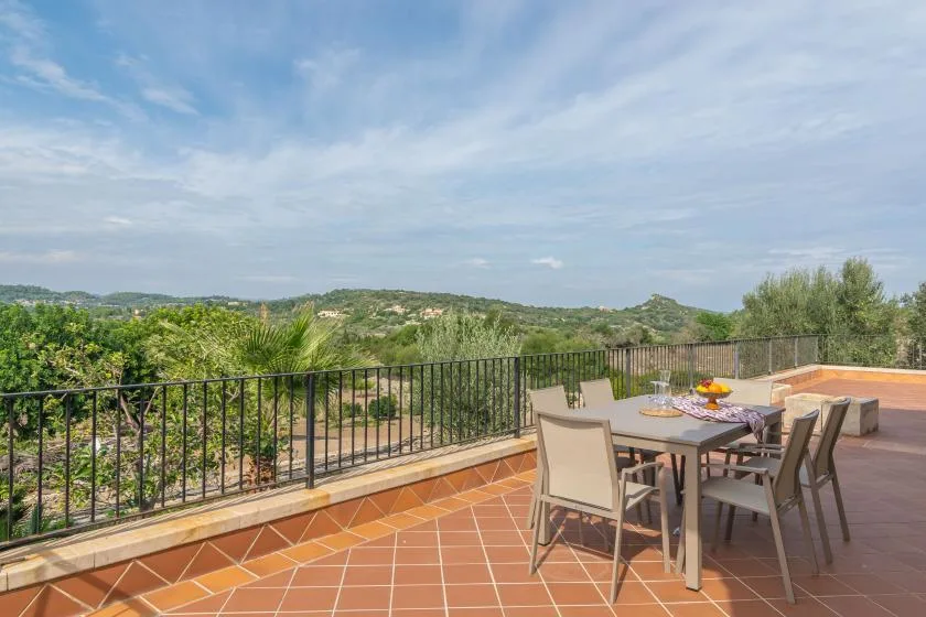 Una zona de comedor en la terraza ofrece vistas a colinas verdes bajo un cielo parcialmente nublado.