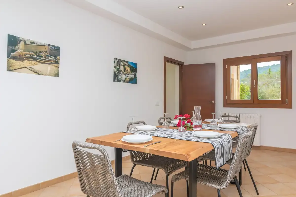 Un comedor con una mesa de madera preparada para comer junto a una ventana.