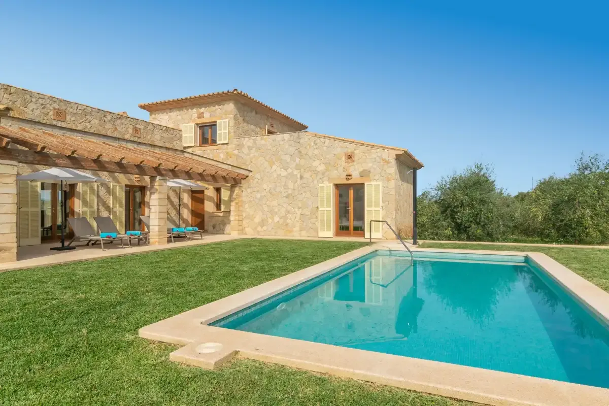 Una casa de piedra se encuentra junto a una piscina y un césped.