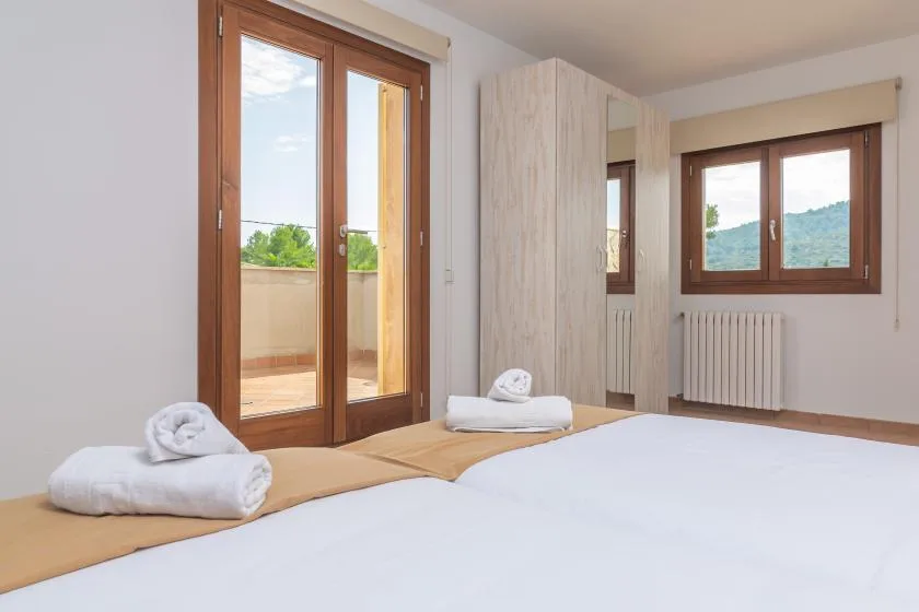 Un dormitorio luminoso con camas hechas y ventanas con marcos de madera.