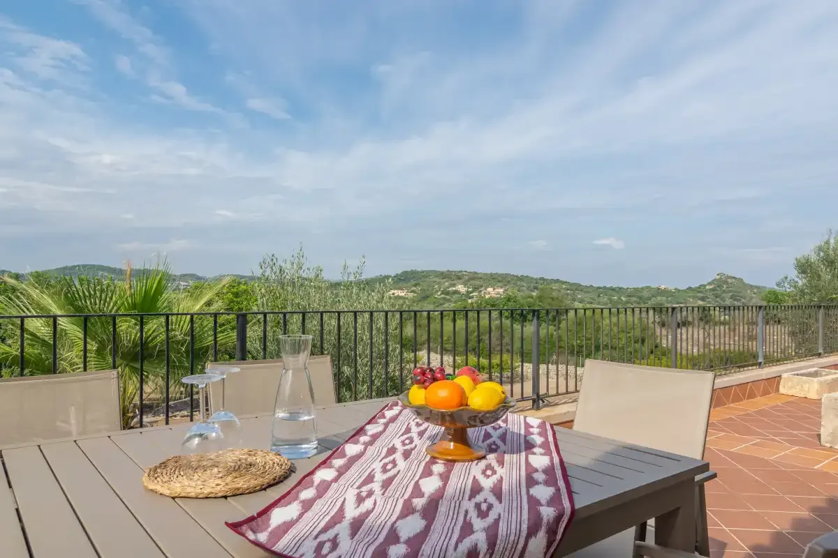Una mesa de comedor en la terraza ofrece vistas a colinas verdes bajo un cielo parcialmente nublado.