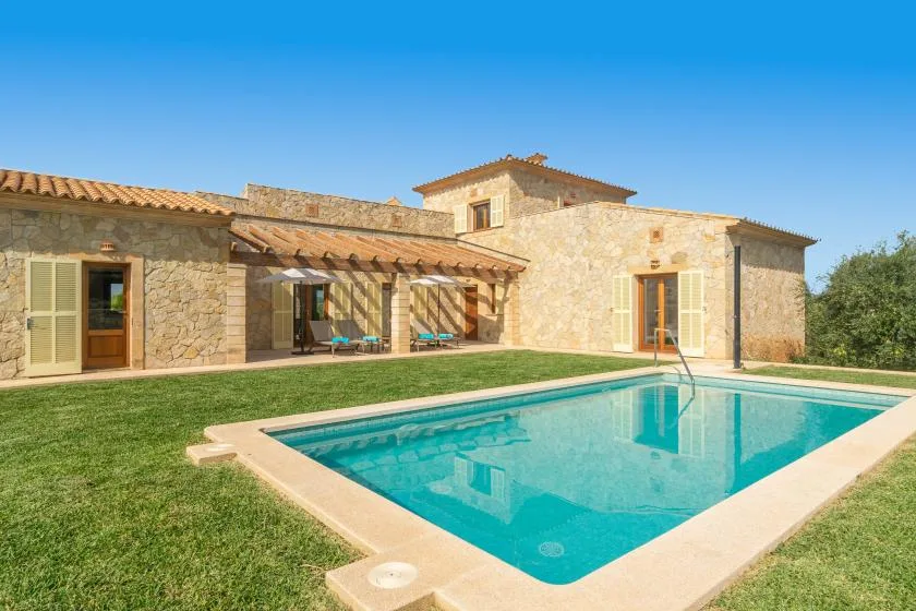 Una casa de piedra da a una piscina rodeada de césped.