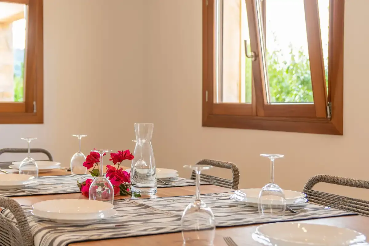 Un comedor con la mesa puesta junto a ventanas iluminadas por el sol.