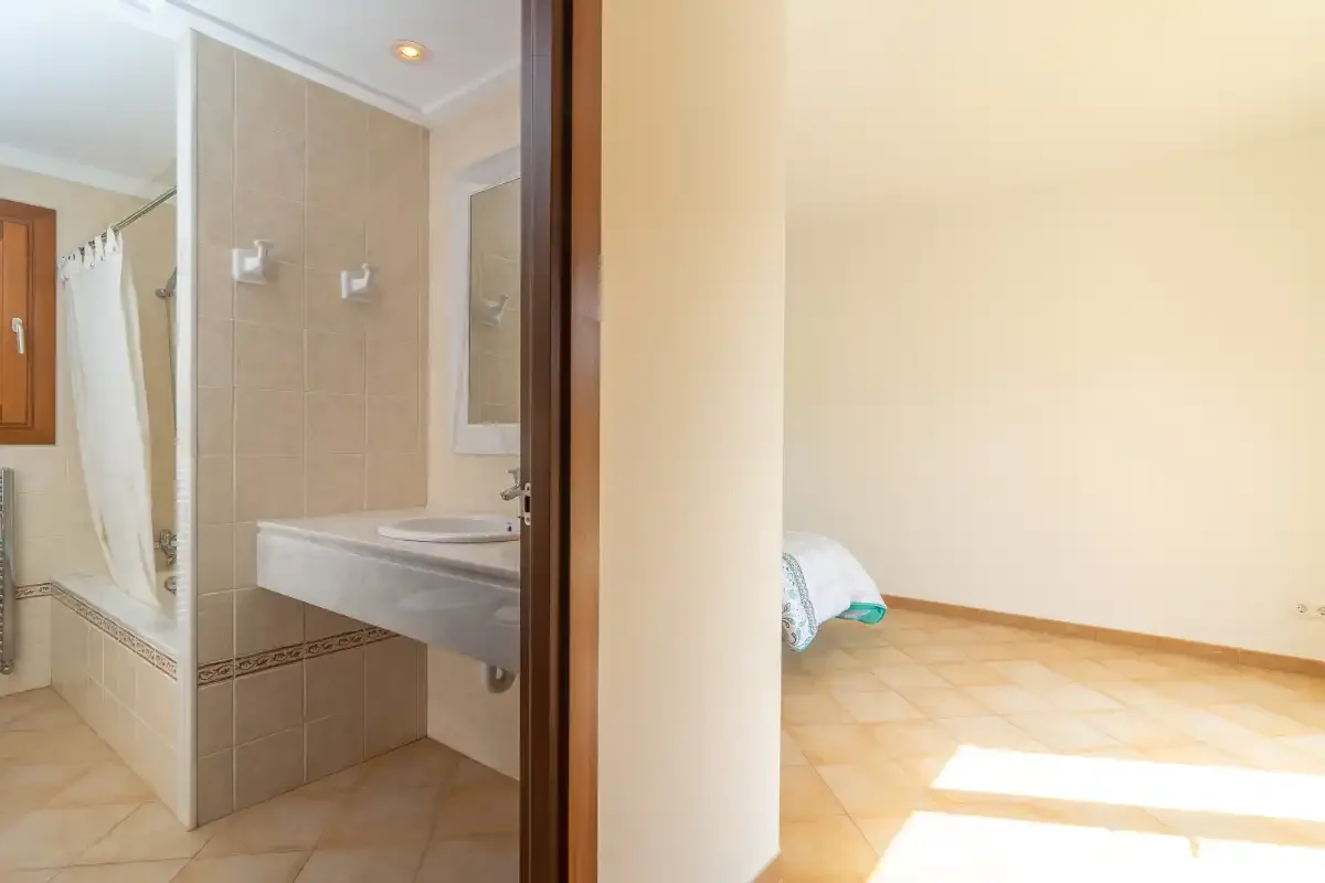 Un baño con ducha y lavabo se abre a una habitación contigua luminosa.