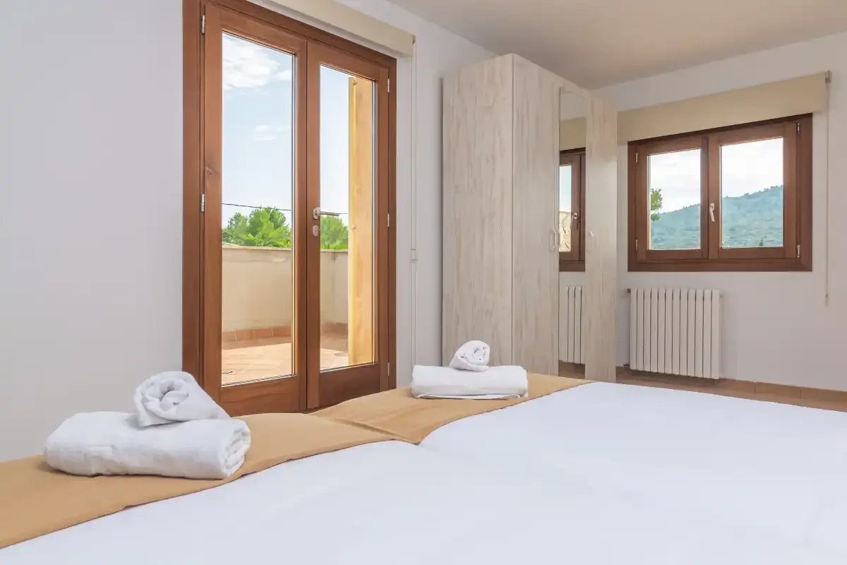 Un dormitorio con una cama, toallas dobladas y ventanas con marcos de madera.