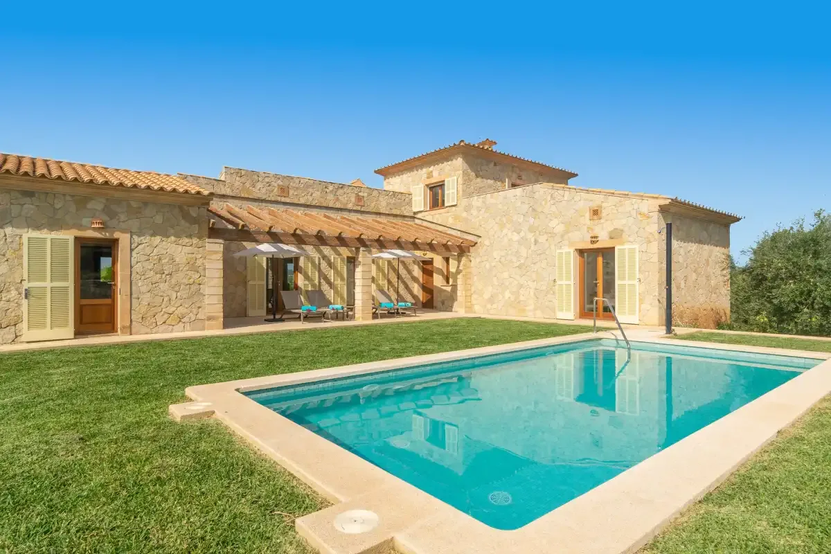 Una casa de piedra está junto a una piscina rectangular y un césped verde.