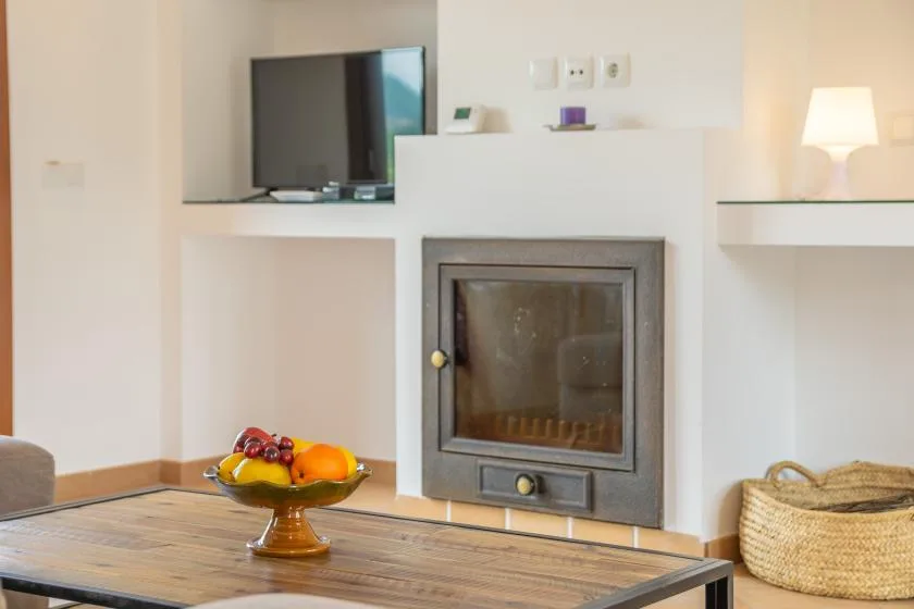 Una sala de estar con chimenea, televisor y un frutero sobre una mesa.