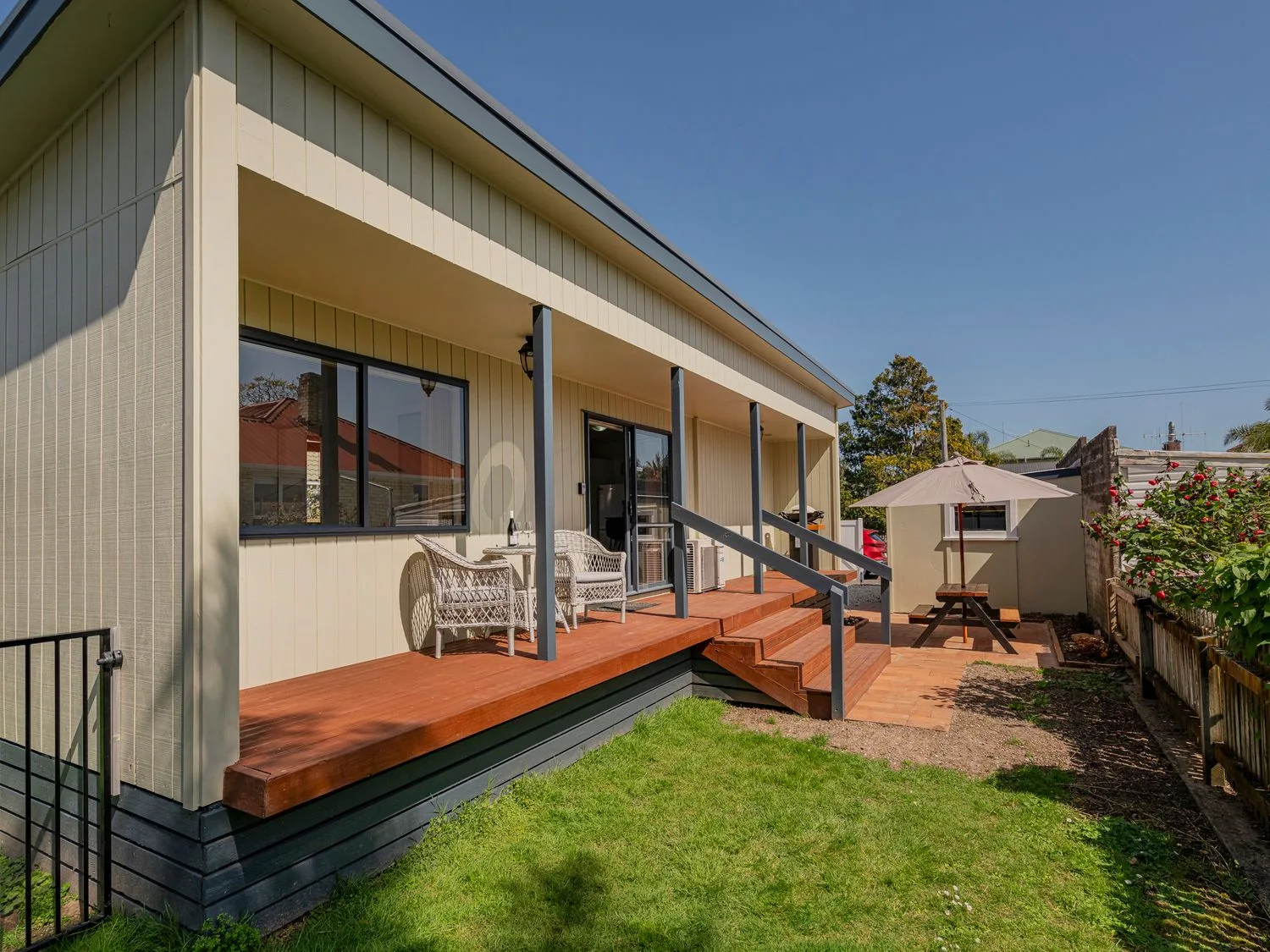 Un patio trasero con una terraza de madera y sillas de mimbre junto a una mesa de pícnic con sombrilla en Gold'n Thames - Thames Holiday Home, en Thames.