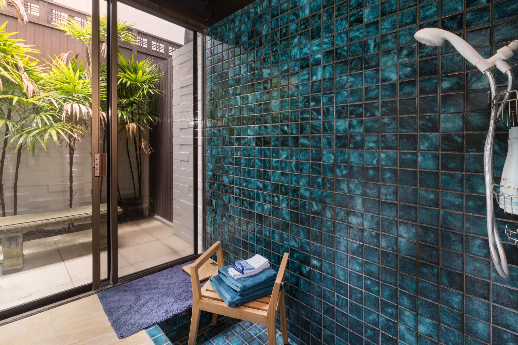 A tiled shower area opens onto a small courtyard with tropical plants.
