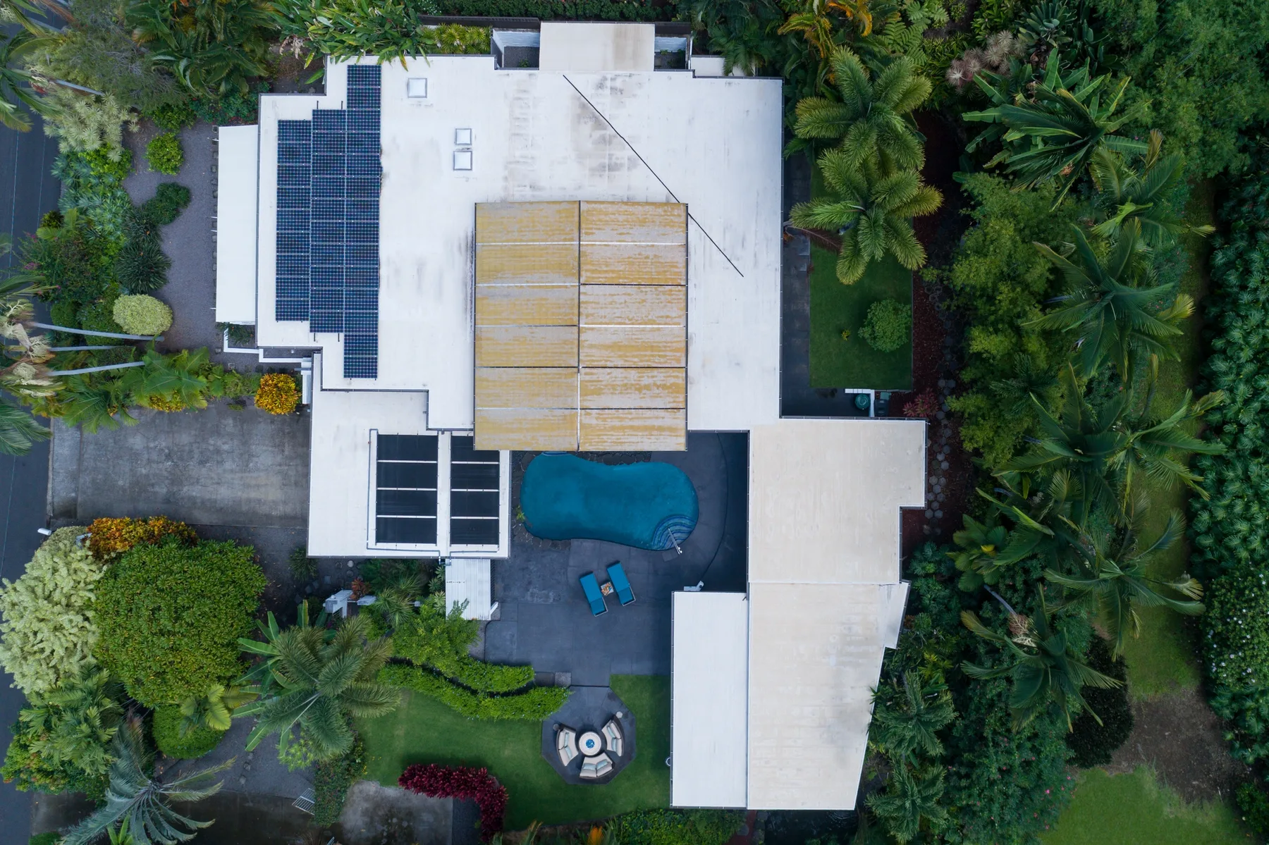 Aerial view of a house with rooftop solar panels, a patio, and surrounding greenery.