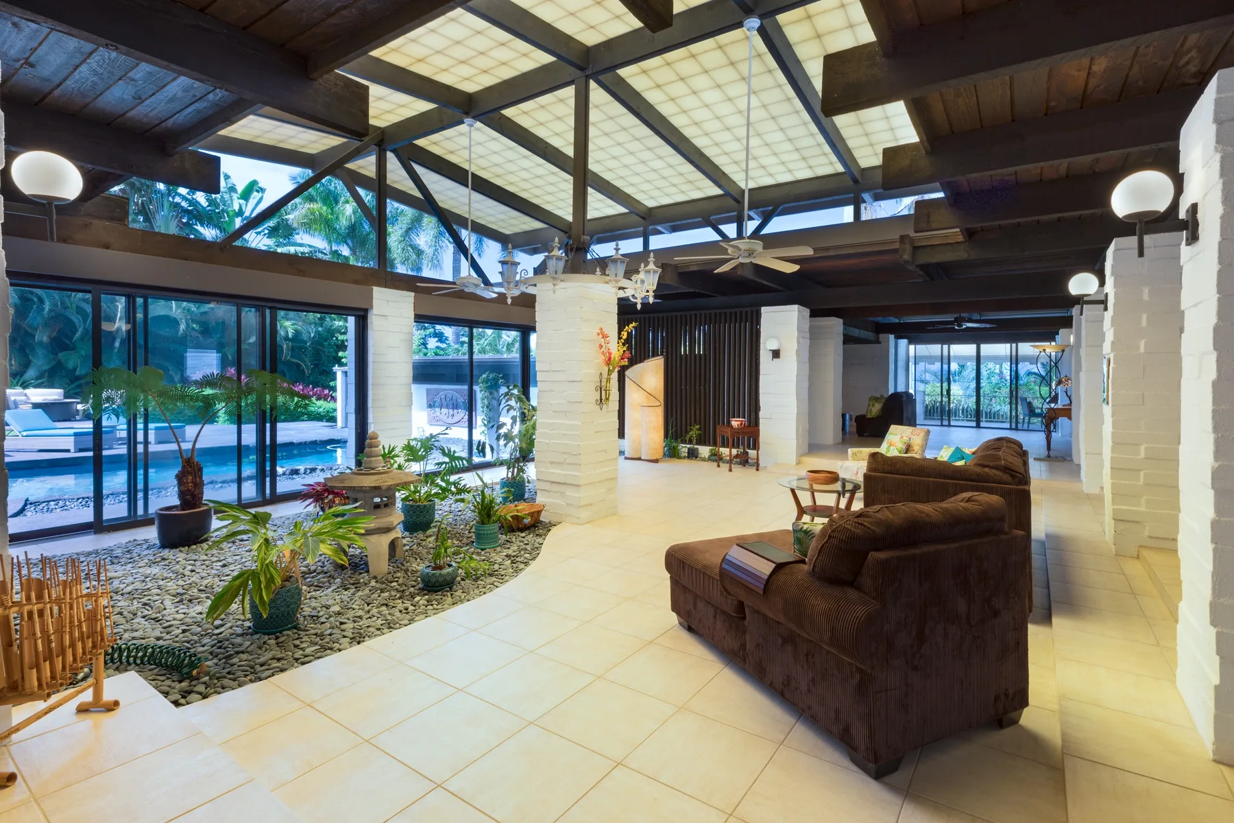 A spacious living area with brown seating, large windows, and indoor plants.