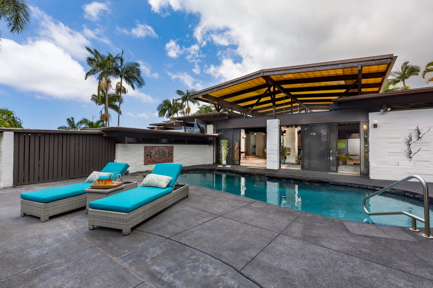 Un patio moderno junto a la piscina, con tumbonas turquesas y una zona exterior cubierta.