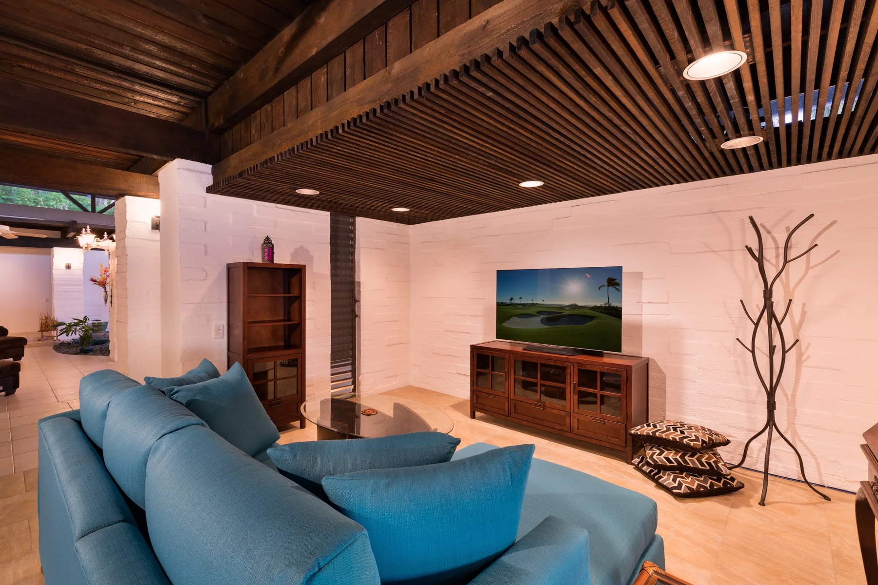 A living room with blue seating, a television, and a dark slatted ceiling.