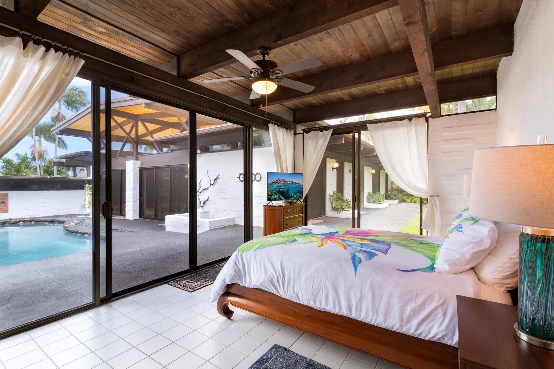 A bedroom with a bed beside large glass doors opening onto a pool area.