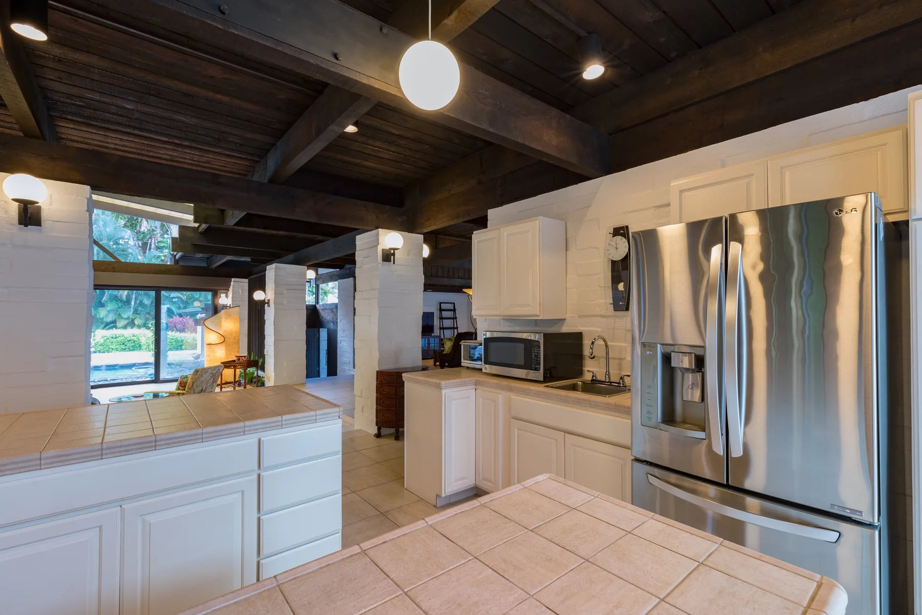 A bright kitchen with white cabinetry and stainless steel appliances beneath a dark beamed ceiling.